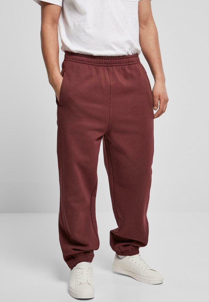 Pantaloni de trening bordo cu un talie elastică, buzunare laterale și manșete elastice, asortați cu adidași albi și un tricou alb simplu.