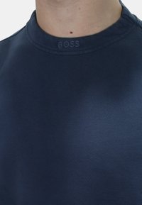 Felpa girocollo blu navy realizzata in materiale a costine, con un logo in rilievo discreto sul colletto e una texture liscia e morbida.