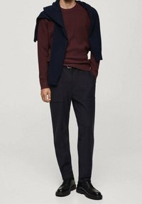 Pull côtelé couleur bordeaux superposé d'un châle bleu marine sur un pantalon sombre avec poches, associé à des chaussures noires à lacets. Tissu lisse et coupe ajustée.