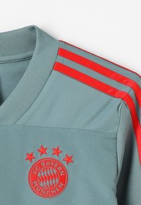 Szaro-czarna koszulka sportowa z czerwonymi akcentami i trzema paskami na ramionach. Posiada haftowane logo z pięcioma gwiazdkami powyżej. Gładka tekstura.