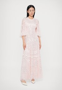 Rochie lungă, roz, cu ornamente din paiete, din material transparent, cu design în straturi. Are mâneci scurte, volanate și decolteu rotund.