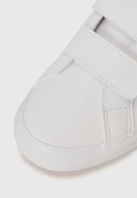 Baskets blanches avec une tige en cuir lisse, bout rond et bandes Velcro. Présentent des coutures simples et une semelle en caoutchouc texturée.