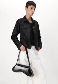 Giacca di pelle nera, top nero e pantaloni a gamba larga bianchi. Una borsa nera lucida dalla forma arrotondata con un dettaglio del logo argentato.