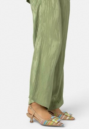 Voeten met kleurrijke geweven slingback-hakken met blokgespen, gecombineerd met losse, gestructureerde lichtgroene broeken.