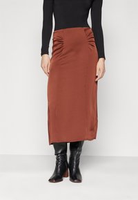 Brun, mid-length skjørt laget av glatt stoff med siderykking, kombinert med svarte lærstøvletter med hæler. Enkelt, tilpasset design.