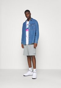 Denim jacket with a front pocket, paired with a white graphic t-shirt and gray shorts, complemented by white sneakers and ankle socks.