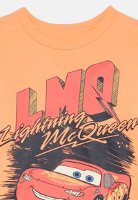 Lightning McQueen racing car with smiling face, red body, and flame decals on an orange background.