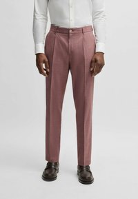 Op maat gemaakte roze broeken met een gestructureerde afwerking, voorzien van plooien en een knoopsluiting op de tailleband. Gepaarde met donkere schoenen.