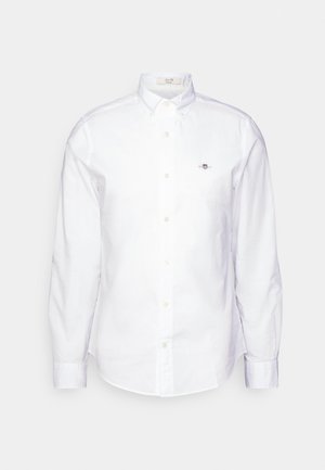 Camisa blanca de manga larga con botones, hecha de algodón, que presenta un cuello clásico, cierre de botones y un pequeño logo bordado en el pecho.