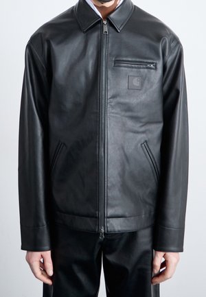 Mand iført en sort læderjakke med lynlås, krave, lynlåslomme på brystet og to sidelommer mod en ensartet lys baggrund.