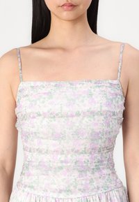 Blomstrete kjole med tynne stropper, laget av et lett stoff i pastellrosa og grønne toner, rynket design og en flytende skjørt.