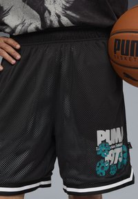 Pantalones cortos de baloncesto de malla negra con un diseño gráfico floral en blanco y teal, que cuentan con una cintura ajustable y franjas laterales. Balón de baloncesto sostenido cerca.