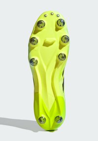 La semelle d'une chaussure de football présente une base en plastique jaune vif avec six pointes métalliques, conçue pour offrir une traction sur les surfaces en herbe.