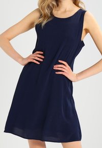 Sininen ilman hihoja mekko, joka on valmistettu kevyestä kankaasta, jossa on pyöreä kaula-aukko ja löysä istuvuus, joka laskeutuu sujuvasti lantion kohdalle.
