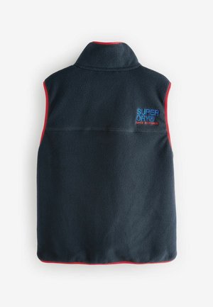 Tumši zila vilnas veste ar augstu apkakli, sarkanu mali un "SUPERDRY" logo zblue. Ievērojama ar gludu tekstūru un vienkāršu, bez piedurknēm dizainu.
