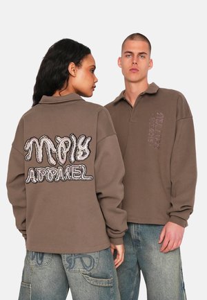 Brown pullover with a collar, featuring embroidered text on the back and sleeve. The fabric appears soft; oversized fit, with long sleeves.