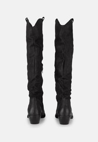 Botas negras hasta la rodilla con acabado de ante, que presentan una forma ajustada, textura elástica y detalles de cremallera para facilitar su uso.
