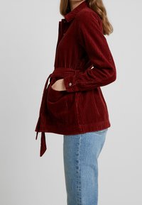 Rode corduroy jas met een getailleerde taille, knopenfront en een grote patchzak. Gestyled over lichtblauwe denim jeans.