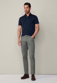Marineblauwe polo, slim-fit lichtgrijze broek en donkerbruine suède schoenen. Eenvoudig ontwerp met een knoopsluiting van drie knopen, geen zichtbare patronen.