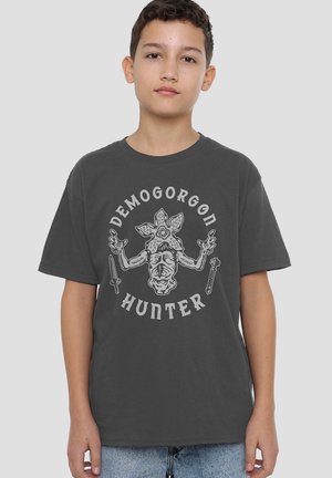 Dunkelgraues Baumwoll-T-Shirt mit einem aufgedruckten Design eines Wesens mit mehreren Armen und dem Text "DEMOGORGON JÄGER" in Weiß.