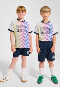 Ungdomsidrottskläder duo: en i en flerfärgad randig t-shirt med marinblå shorts, den andra i en liknande stil. Både bär vita och gröna sneakers.