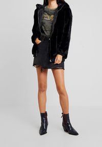 Sort faux fur zip-jakke, camo t-shirt med gul tekst, nedslidt sort denimnederdel og mørke, lakerede ankelstøvler med spids tå.