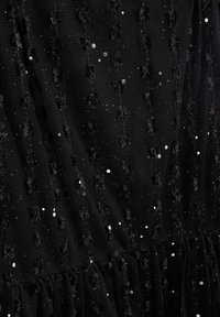 Černé šaty s texturovanou síťovinou, zdobené flitry a tkanými květinovými akcenty, které vytvářejí vrstevnatý efekt podél lemu a povrchu.