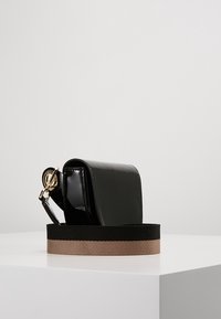 Černá lakovaná kožená taška obdélníkového tvaru, se zlatými doplňky a odnímatelným popruhem s barevným blokováním černé a hnědé barvy.