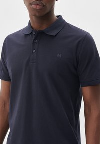 Námornícky modrá polo košeľa vyrobená z texturovanej bavlny, s trojitou gombíkovou légou a decentným logom na hrudi. Krátke rukávy s žebrovanými manžetami.