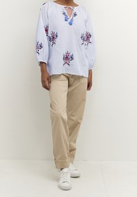 Modrá a bílá pruhovaná blůza s květinovou výšivkou, zavazovací detaily u výstřihu a nabíranými rukávy. V kombinaci s béžovými kalhotami a bílými teniskami.