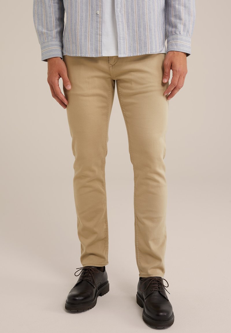 Beige slim-fit chinos i en bomullsblandning, med en slät yta och rena linjer, matchade med svarta snörskor.