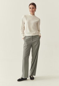 Pull crème clair, cintré à la taille, associé à un pantalon gris à larges jambes. Chaussures noires avec lacets camel et texture lisse. Design minimaliste.