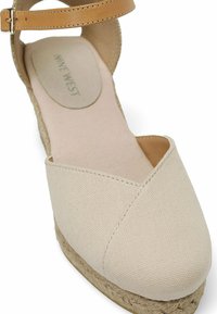 Beige canvas espadrille met een wiggenhak en enkelbandje. Geverfd materiaal en jute zool; ronde neus met een crossover ontwerp.