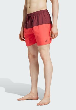 Bañadores rojos y burdeos hechos de un tejido ligero. Cuentan con una cinturilla elástica con cordón y un logo de Adidas en el lateral.