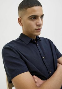 Camisa de manga corta azul marino de lino, con cuello abotonado y botones de madera, de corte relajado.