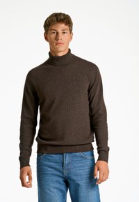 Brun polotröja av texturerat stickat tyg, med en åtsittande design och ribbade ärmslut, kombinerad med blå jeans.
