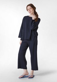 Marine loungewear set bestaande uit een langemouwen top en wijde broek, gemaakt van zachte stof. Draagt met blauwe badslippers.