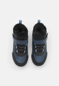 Pár modrých a černých zimních bot s černou kožešinovou podšívkou, elastickými tkaničkami a suchými zipy, pohled zeshora na bílém pozadí.