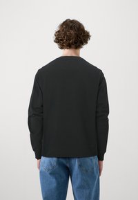 Svart långärmad sweatshirt med rund halsringning, tillverkad av ett enhetligt tyg. Matchas med ljusblå denimjeans med bakfickor.