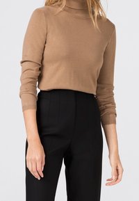 Světlý hnědý rolák z měkké pletené tkaniny, s dlouhými rukávy a přiléhavým střihem, doplněný černými kalhotami s vysokým pasem.