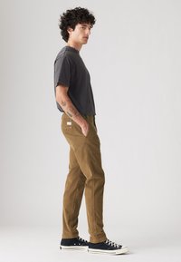 Camiseta de manga corta gris oscuro combinada con pantalones de pana color beige. El modelo lleva zapatillas negras con suelas blancas. Diseño sencillo y ajuste relajado.