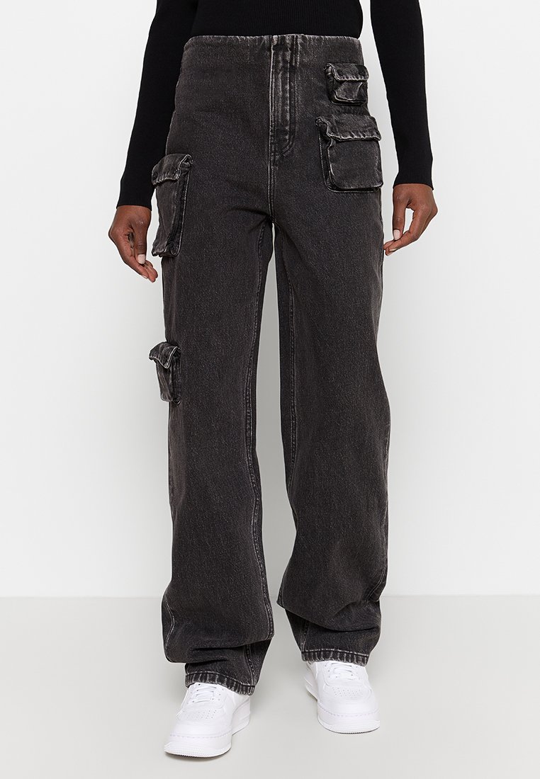 Pantaloni cargo in denim nero con una vestibilità ampia, multiple tasche e orli sfrangiati. Indossati con sneaker bianche per un contrasto.