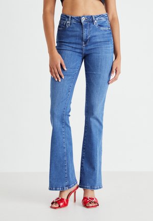 Jean flare taille haute en denim bleu moyen avec une finition lisse. Dispose d'un design à cinq poches et de passants de ceinture, associé à des sandales à talons rouges.