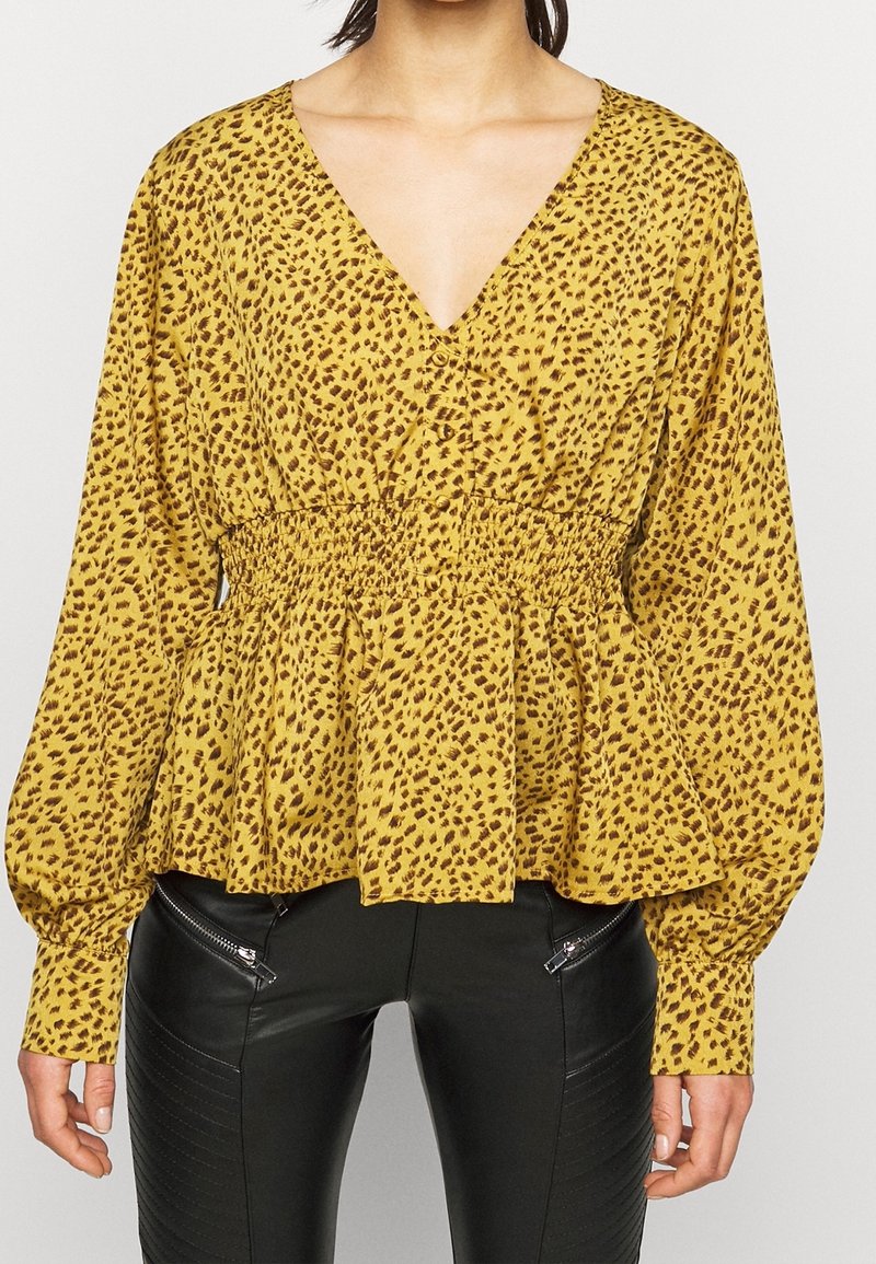 Gul blus med leopardmönster, djup V-ringning och puffärmar. Har elastisk midja och flytande peplumslits. Kombinerad med svarta läderbyxor.