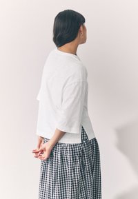 Maglietta bianca a maniche corte con vestibilità larga e spacchi laterali, abbinata a una gonna a quadretti blu navy e bianca.