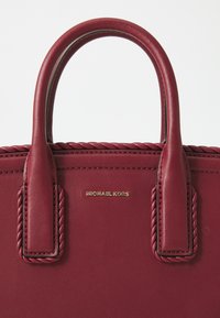 Burgundy läderhandväska med dubbla, flätade handtag och en gold "MICHAEL KORS"-logotyp. Slät textur och strukturerad design.