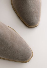 Grå ruskinds-ankelstøvler med spids snude og lav hæl, der har en glat tekstur og subtile syninger langs kanterne.