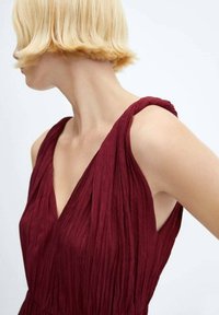 Robe sans manches bordeaux avec une texture plissée, dotée de larges bretelles et d'un décolleté en V profond. Fini en tissu lisse.