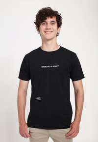 Schwarzes Baumwoll-T-Shirt mit dem Text "DRENCHED IN MONET" in Weiß auf der Vorderseite, mit einem kleinen Logo unten links.