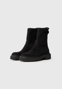 Bottines en daim noir avec une tige texturée, un bout rond et une semelle en caoutchouc épaisse. Dispose d'une languette à l'arrière pour un enfilage facile.